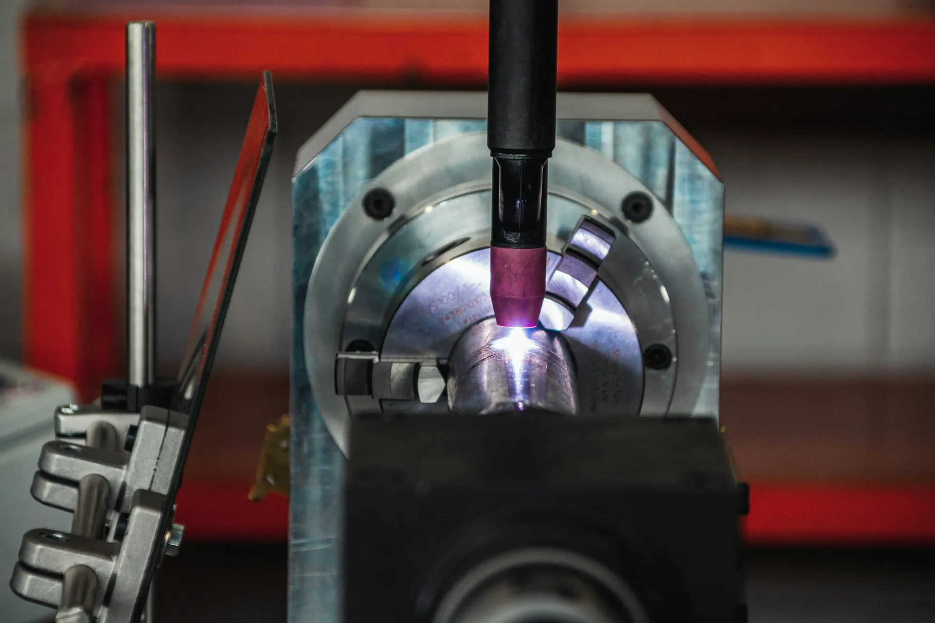A welding cell holds programs, taught paths and parameters just as a PLC does, and it is far more likely to be missing from the backup plan. Automated welding torch glowing over a part clamped in a rotary chuck fixture
