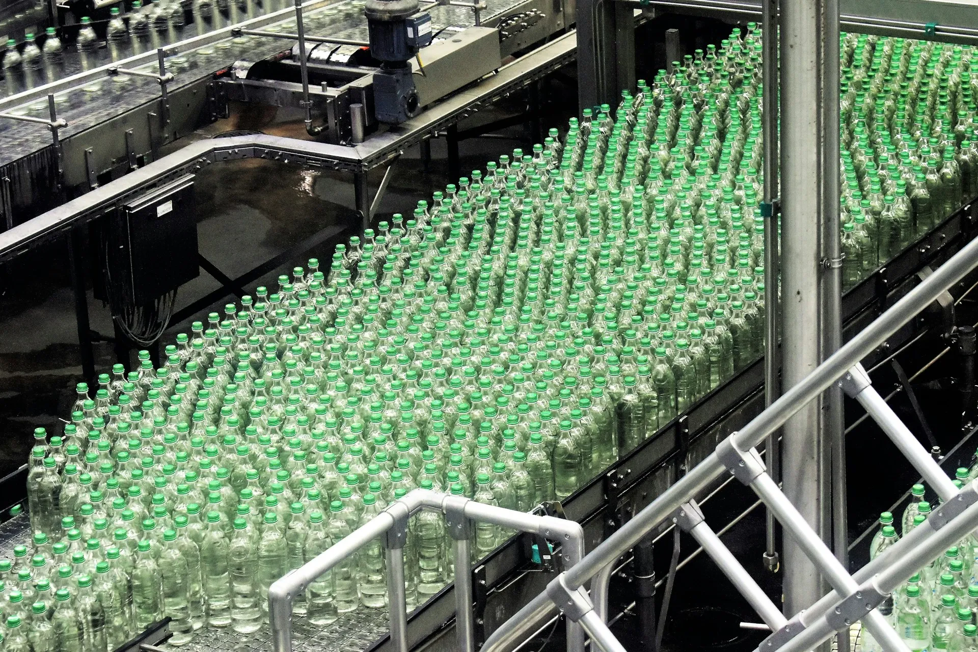 A high-speed line produces thousands of events a minute. Only a summarised, governed subset belongs on the enterprise backbone; the rest stays in the plant. Hundreds of green glass bottles crowding a stainless steel conveyor on a bottling line