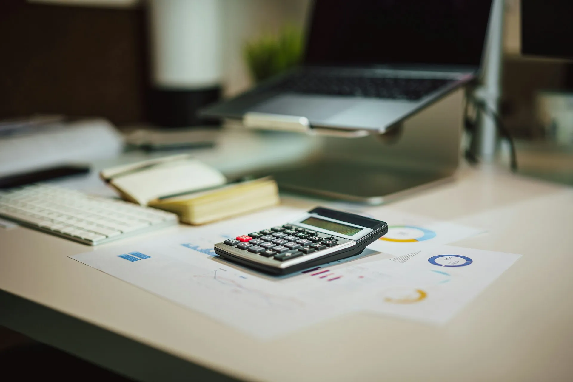 The licence is one line of the business case. Environments, disaster recovery, infrastructure and the people who run the brokers usually decide the total. Calculator resting on printed charts and reports on an office desk beside a keyboard and laptop