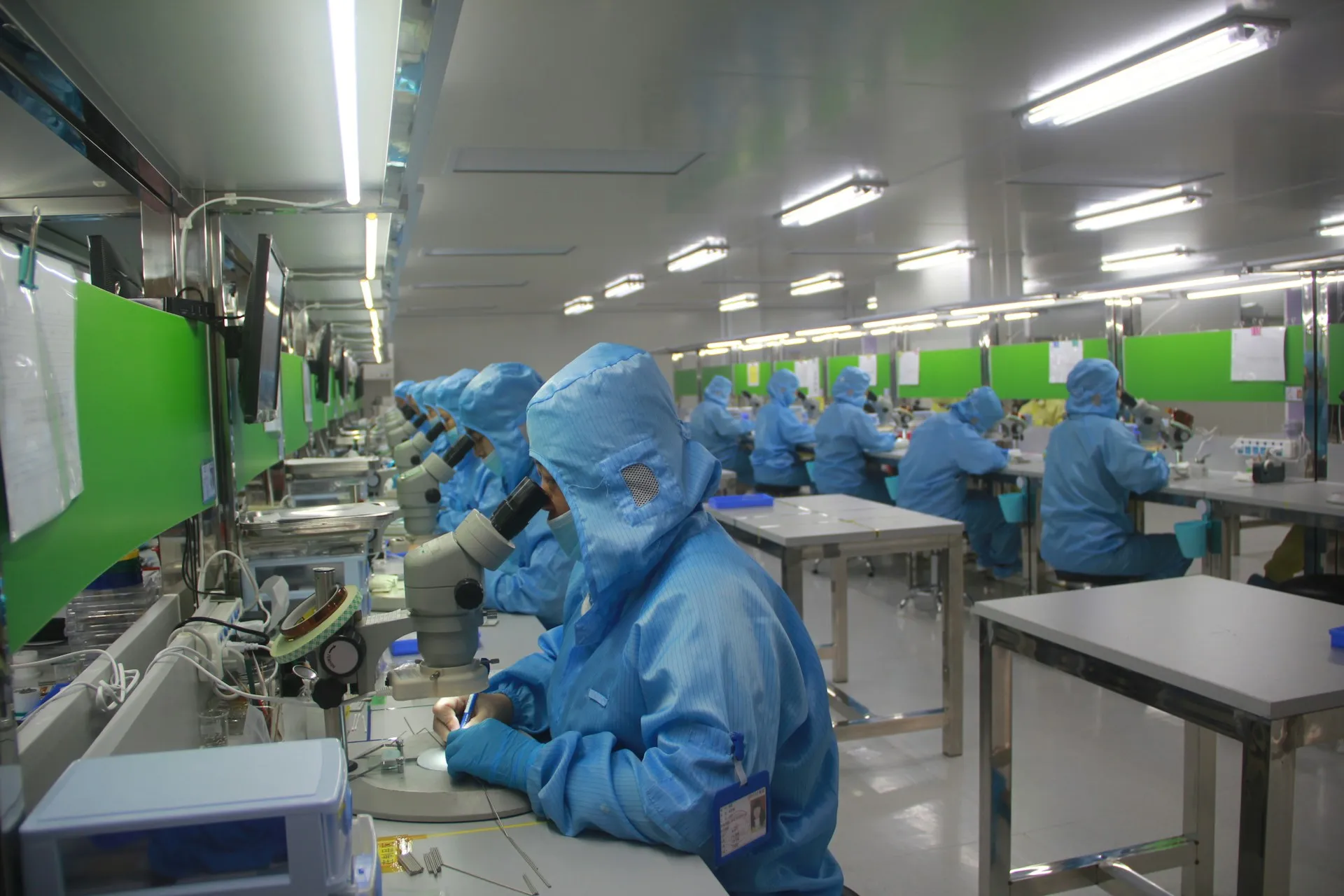 Gowning and procedures control what enters the room. They cannot show whether the code on the equipment is still the version that was qualified; only a compare against the device can. Operators in full cleanroom suits working at microscopes along a long production hall