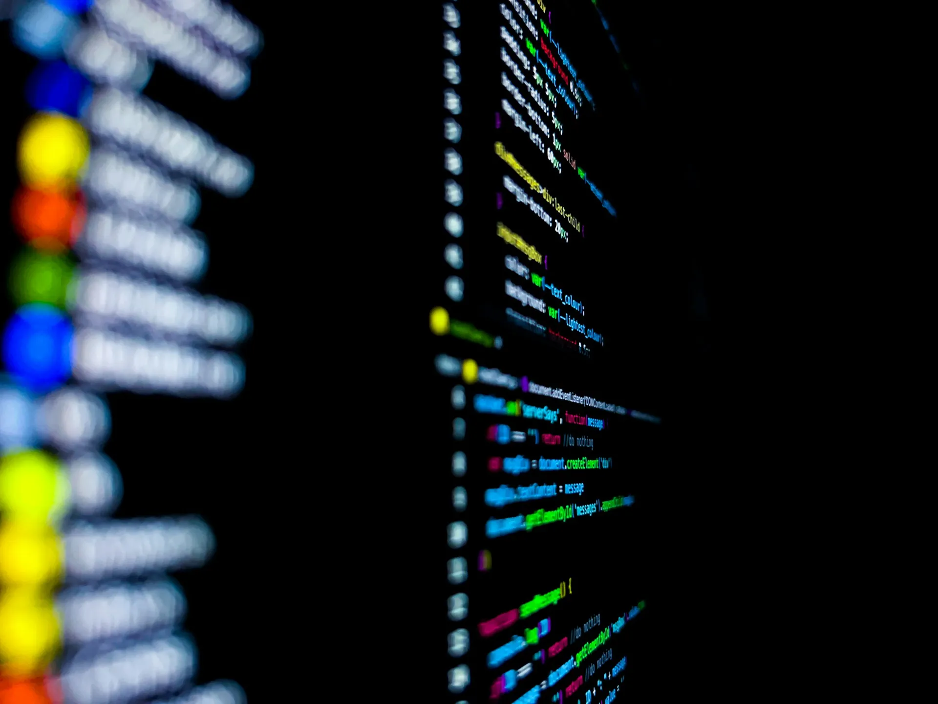 Generated code is only trustworthy when the contract it came from is reviewed and versioned like the code itself. Close-up of colourful source code on a dark monitor with a blurred sidebar in the foreground