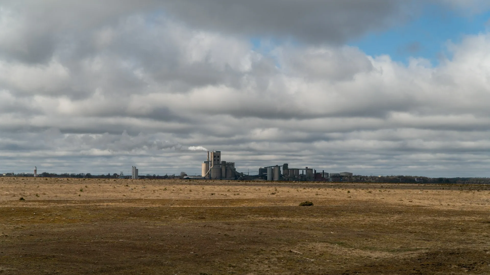 A cloud region is a physical place. Put each broker service close to the systems that produce or consume most of its events, and pay attention to what crosses the boundary. Wide open plain under a heavy cloudy sky with distant industrial buildings on the horizon