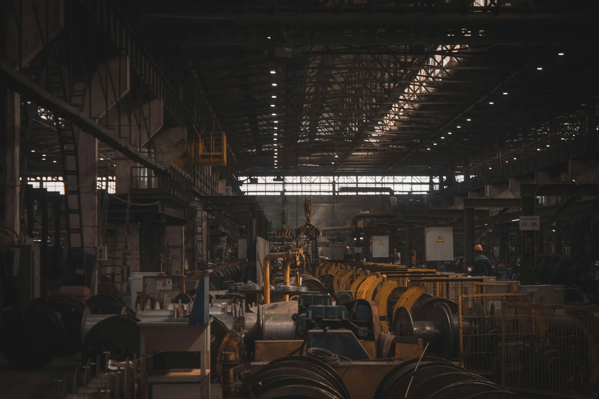 Dark heavy industry factory hall with rows of cable drums and machinery under overhead lights