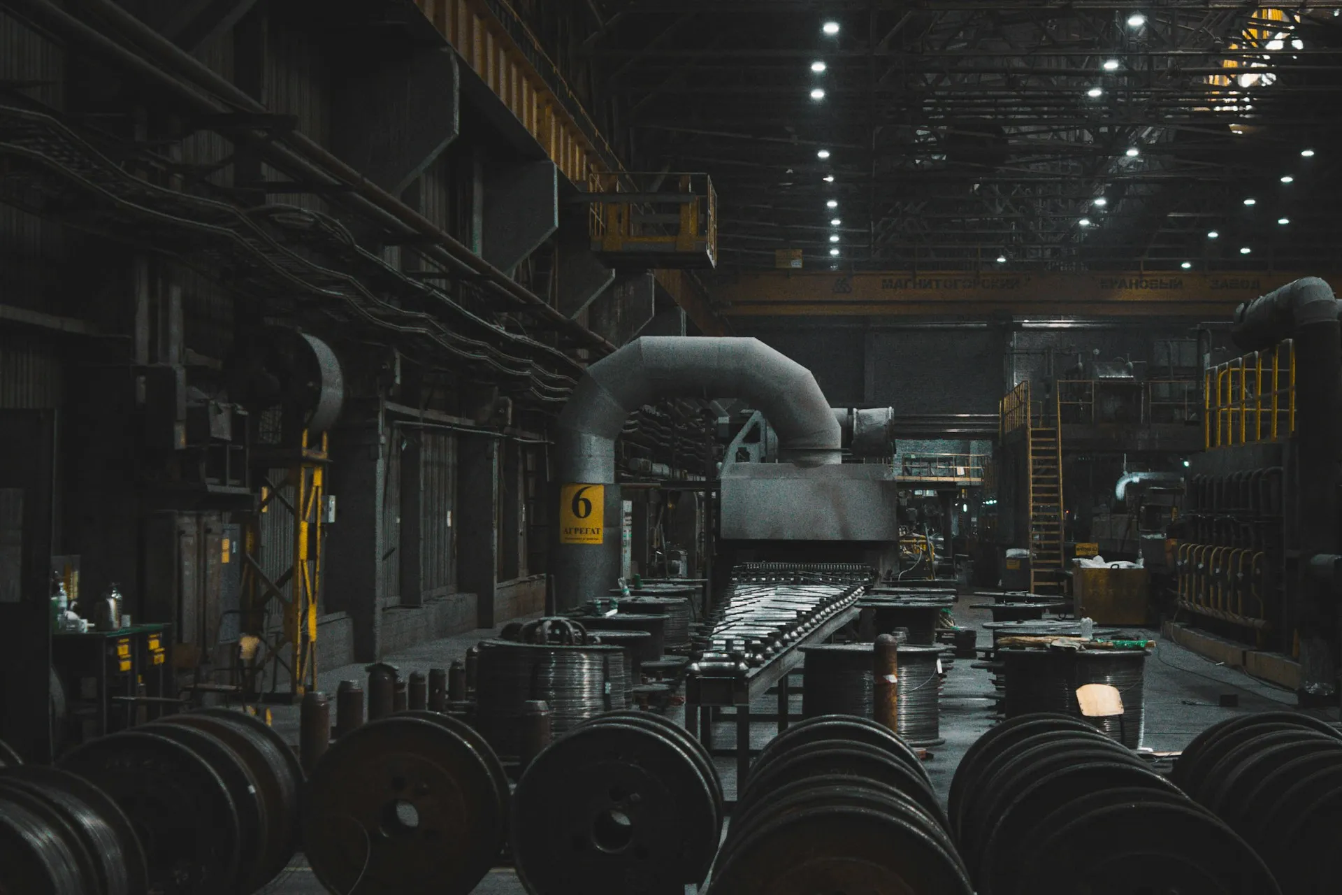 A ransomware outage often looks like this: the controllers are intact, but with no screens and no engineering tools nobody can safely run the line. Dim, quiet steel plant hall with idle processing lines, stacked coils and overhead lighting