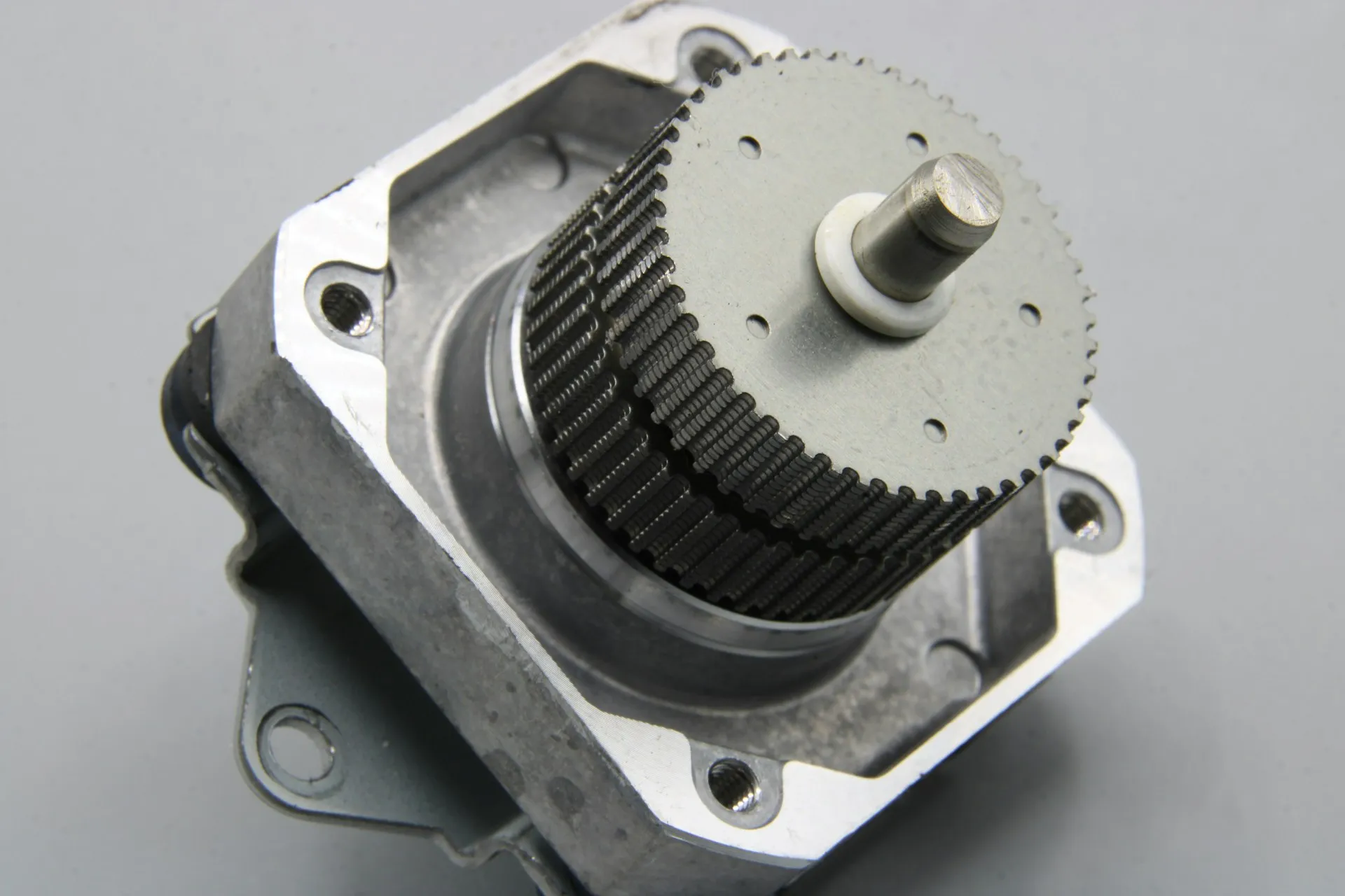 Small motor partly disassembled on a grey surface, showing the toothed rotor and mounting flange