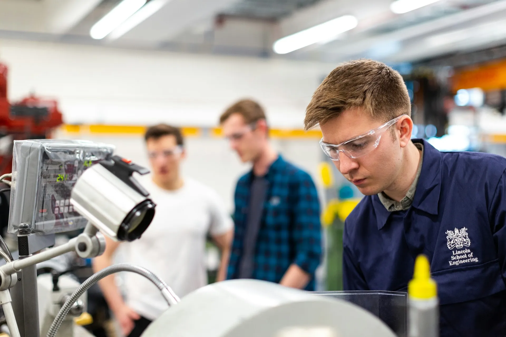 A FAT is witnessed testing: the end user watches every step run against the protocol, at the shop, while defects are still cheap to fix. Three engineers gathered around a machine on a test bench in a fabrication shop, one inspecting it closely