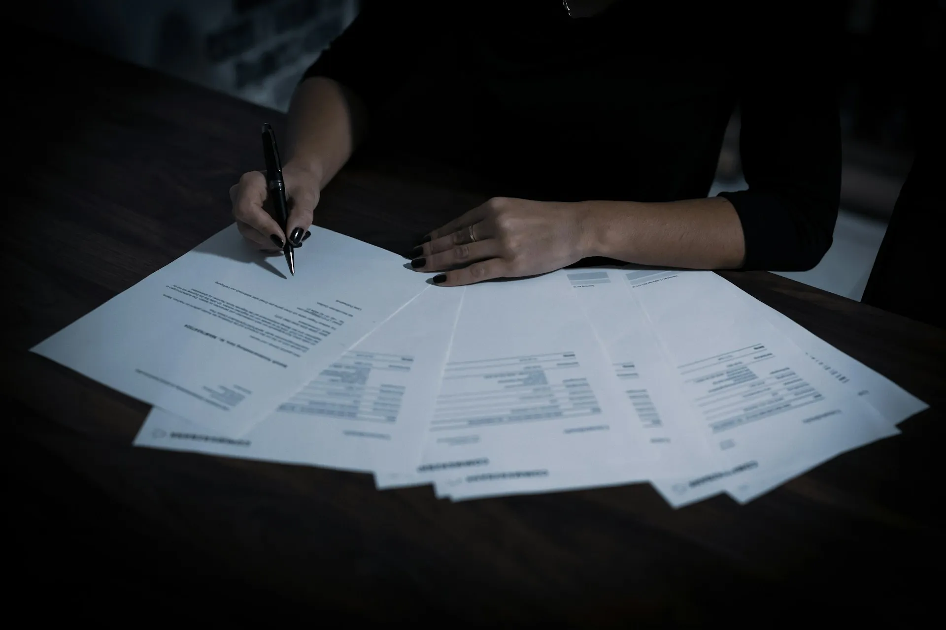 Every answer that is not in writing before signature becomes a negotiation at renewal, so get the device rule and the tier features into the contract. Hand signing one of several printed agreement pages fanned across a dark table