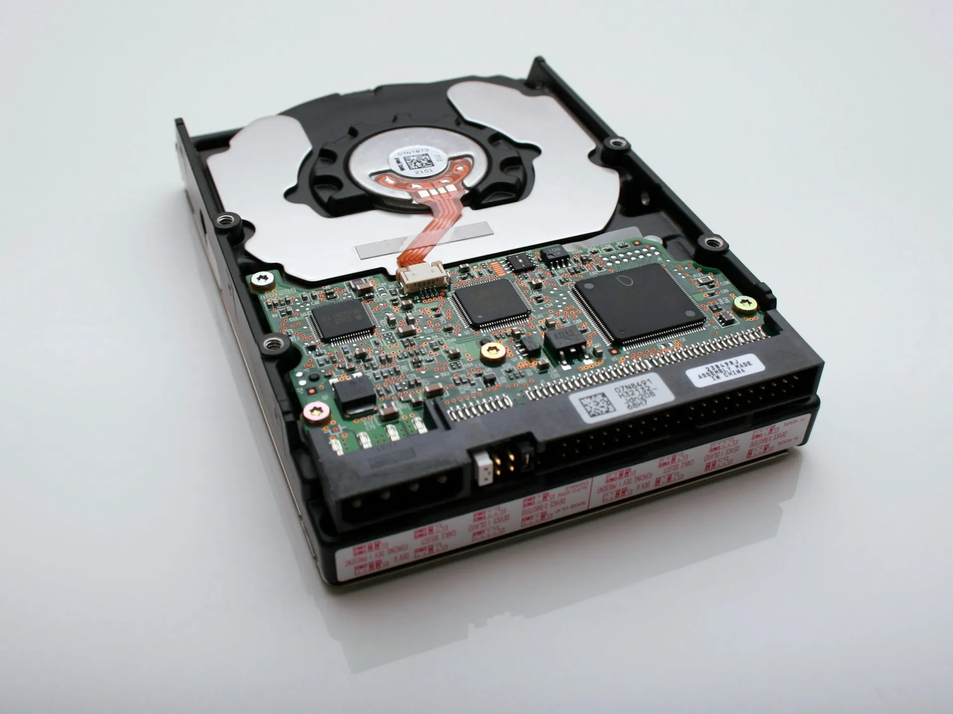 A backup is one physical object until it is copied: a single disk or server holding every program is a single point of failure. Hard disk drive on a white surface showing its exposed circuit board, connectors and spindle cover
