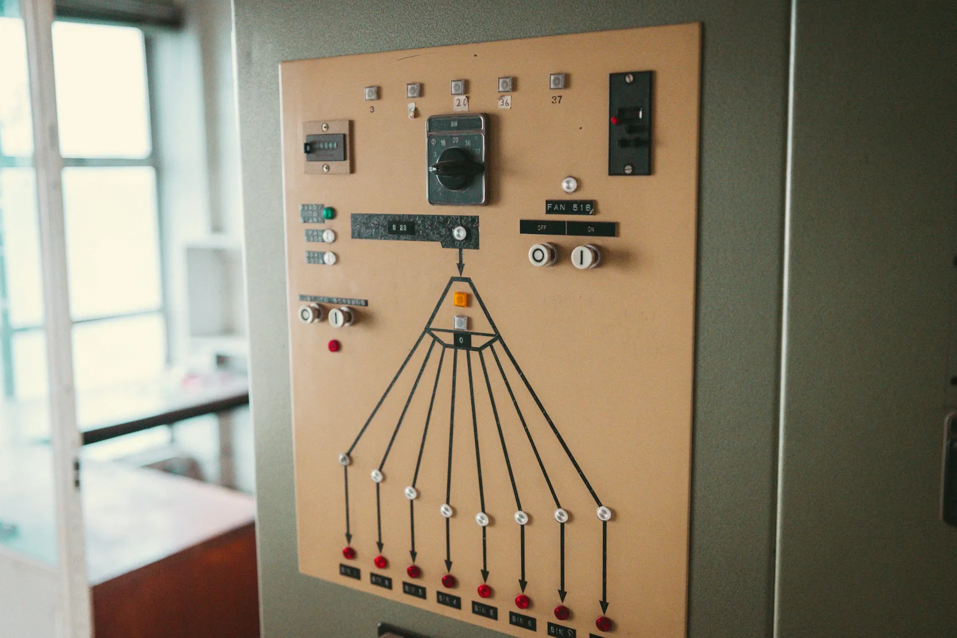 The first PLCs replaced panels like this one, and they inherited its habit: meaning lived in drawings and addresses, not in the program. Beige hardwired control panel with a rotary selector, pushbuttons and a drawn line diagram to indicator lamps