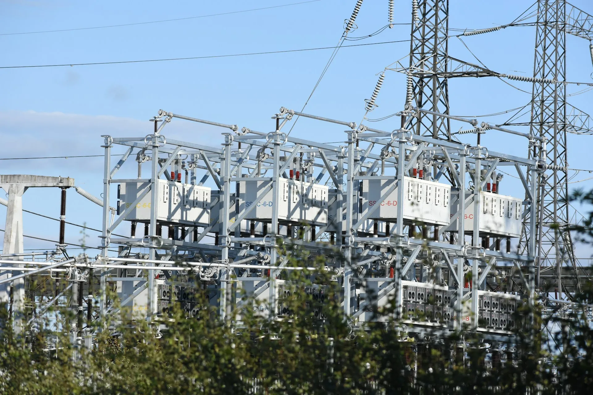 Energy was always in scope; NIS2's annexes now reach machinery, electronics, food and chemicals plants too, and every one of them owes backup, recovery and incident handling for its OT. High-voltage substation switchgear on steel lattice structures behind green trees