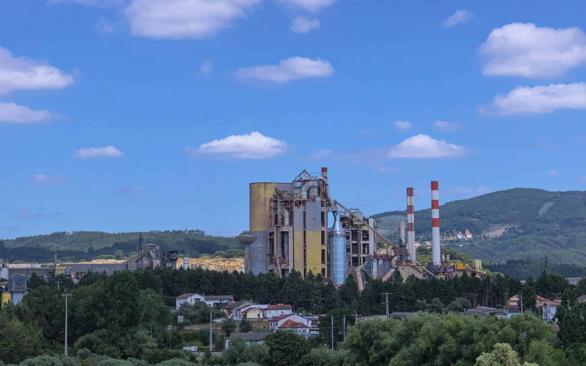 Plant events can stay local by default, while only the streams that cloud analytics actually subscribes to leave the site through the same mesh. Industrial plant with tall chimneys beneath a blue sky with scattered white clouds