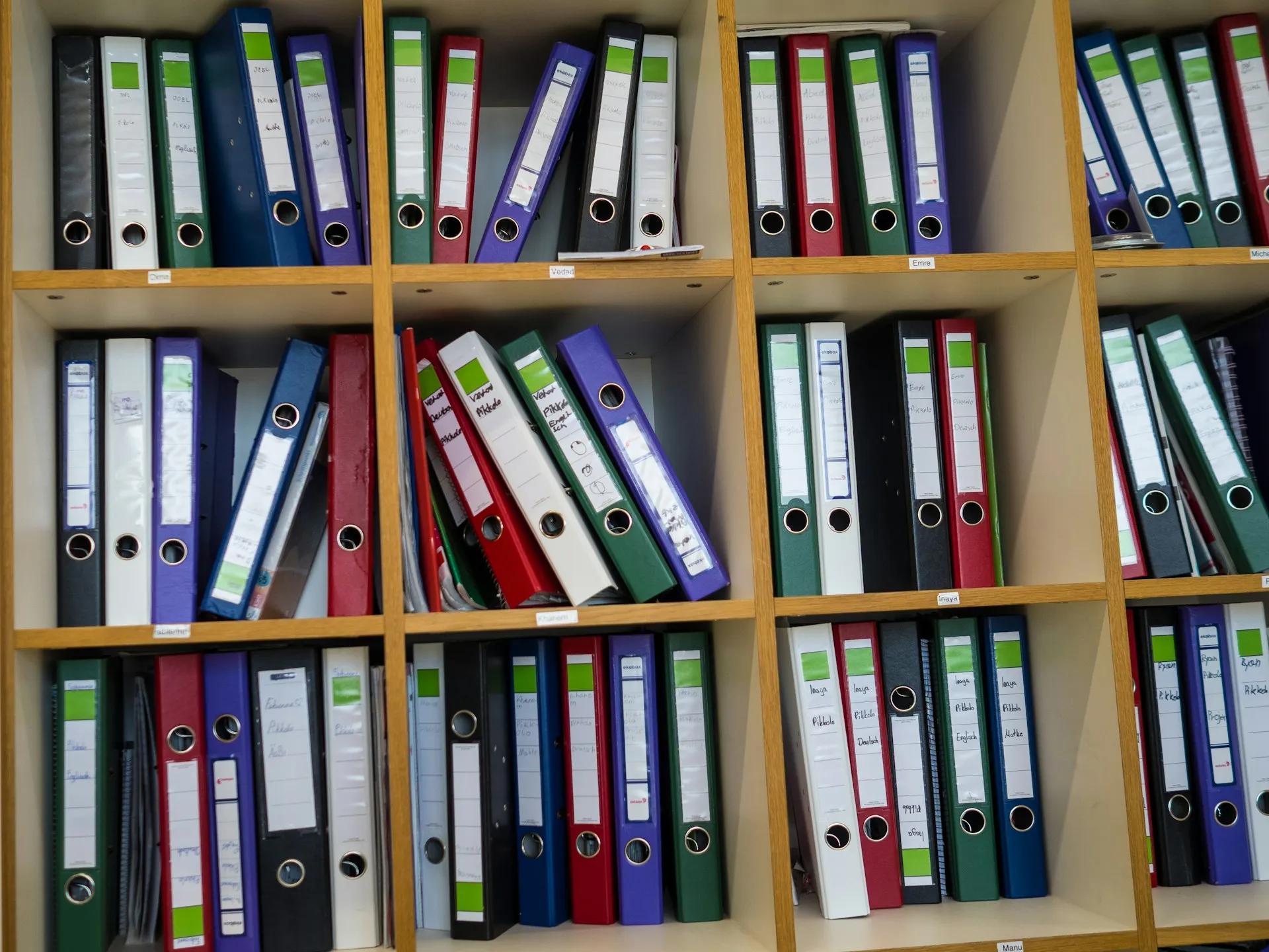 Shelves of colour-coded ring binders with handwritten spine labels in an office