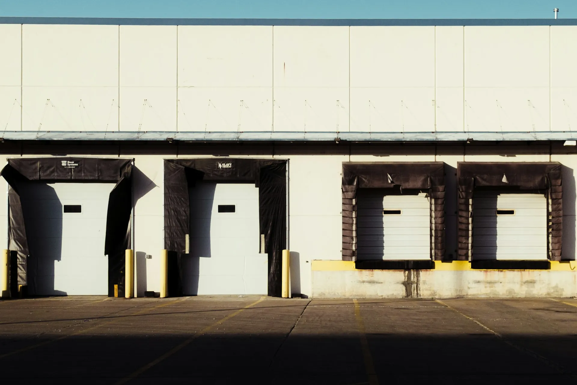 Each consuming system gets its own dock. A delay at one door holds up only that door's deliveries, never the others. Row of loading dock doors along the side of a commercial building