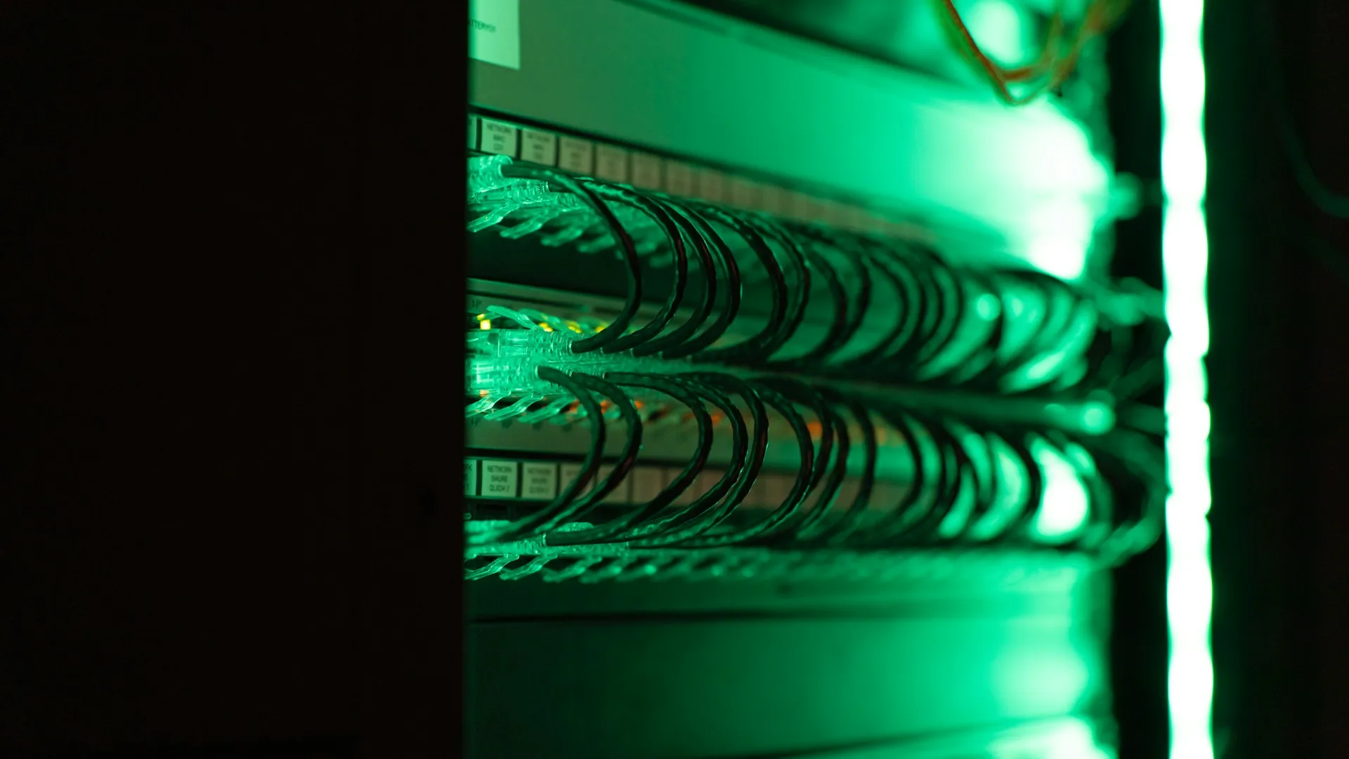 Kafka belongs where servers, storage and an operations team already are. Its value is history and fan-out to data platforms, not the last metre to a machine. Patch cables glowing green inside a dark network rack in a server room