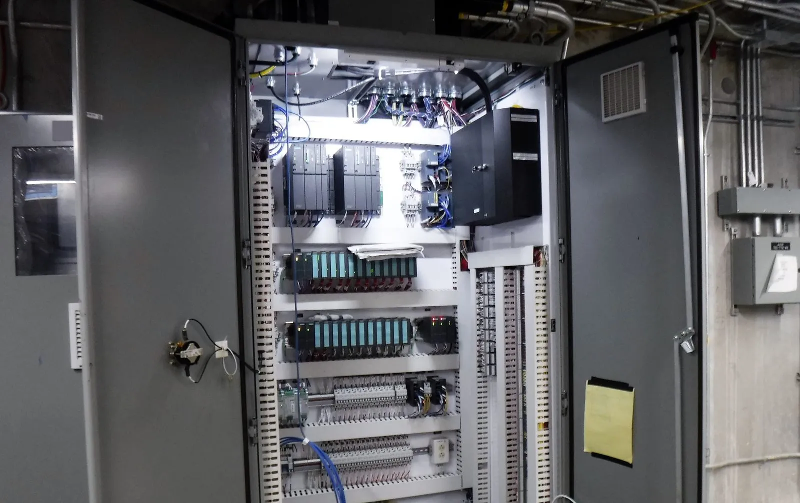 Open control cabinet with controller modules, I/O racks, terminal strips and tidy wiring under bright light