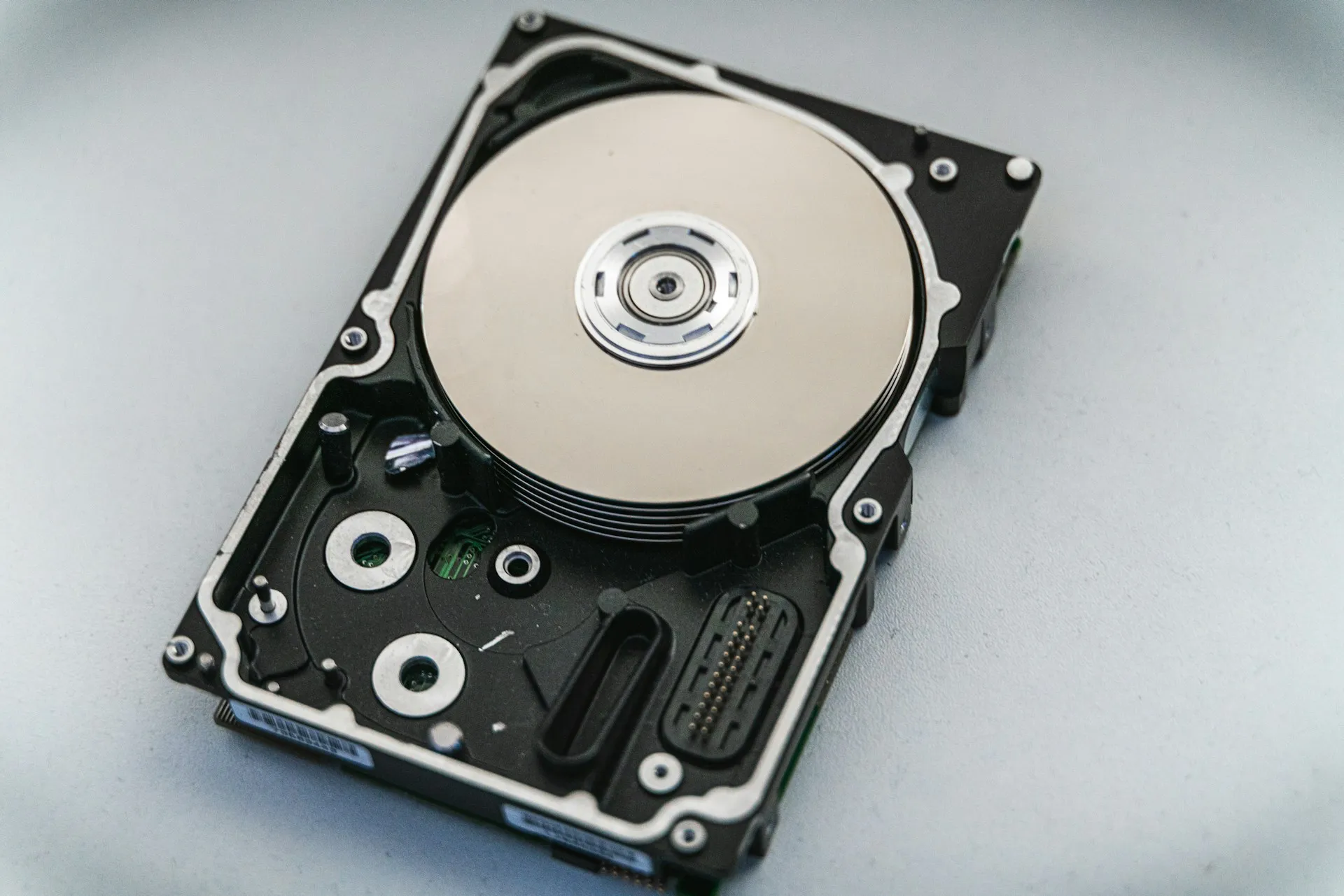 A disk image can put a server back, but the logic that runs the line lives in the controller's memory, so it has to be read from the device itself. Opened hard disk drive showing the platter and read head assembly on a pale surface