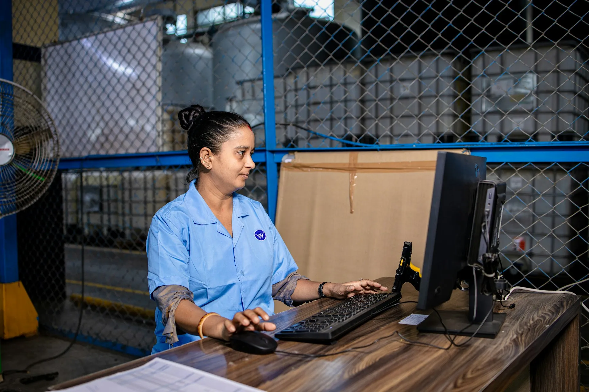 The value of one console is not convenience. It is that the person on shift can see every broker's state in one place instead of logging into each service while a line waits. Operator in a blue work shirt using a desktop computer at a workstation on a plant floor