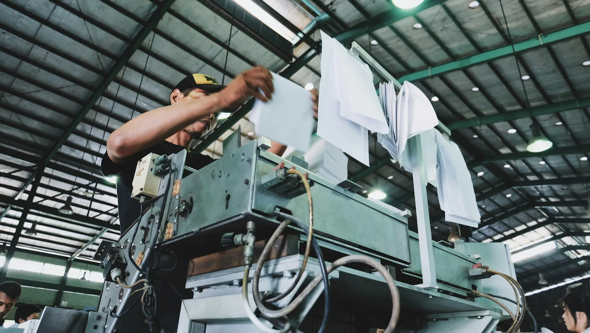 A signed sheet on the machine proves somebody did the work. Only a compare against the approved version proves what the work changed in the code. Worker standing on a machine sorting papers clipped above it in a large factory hall