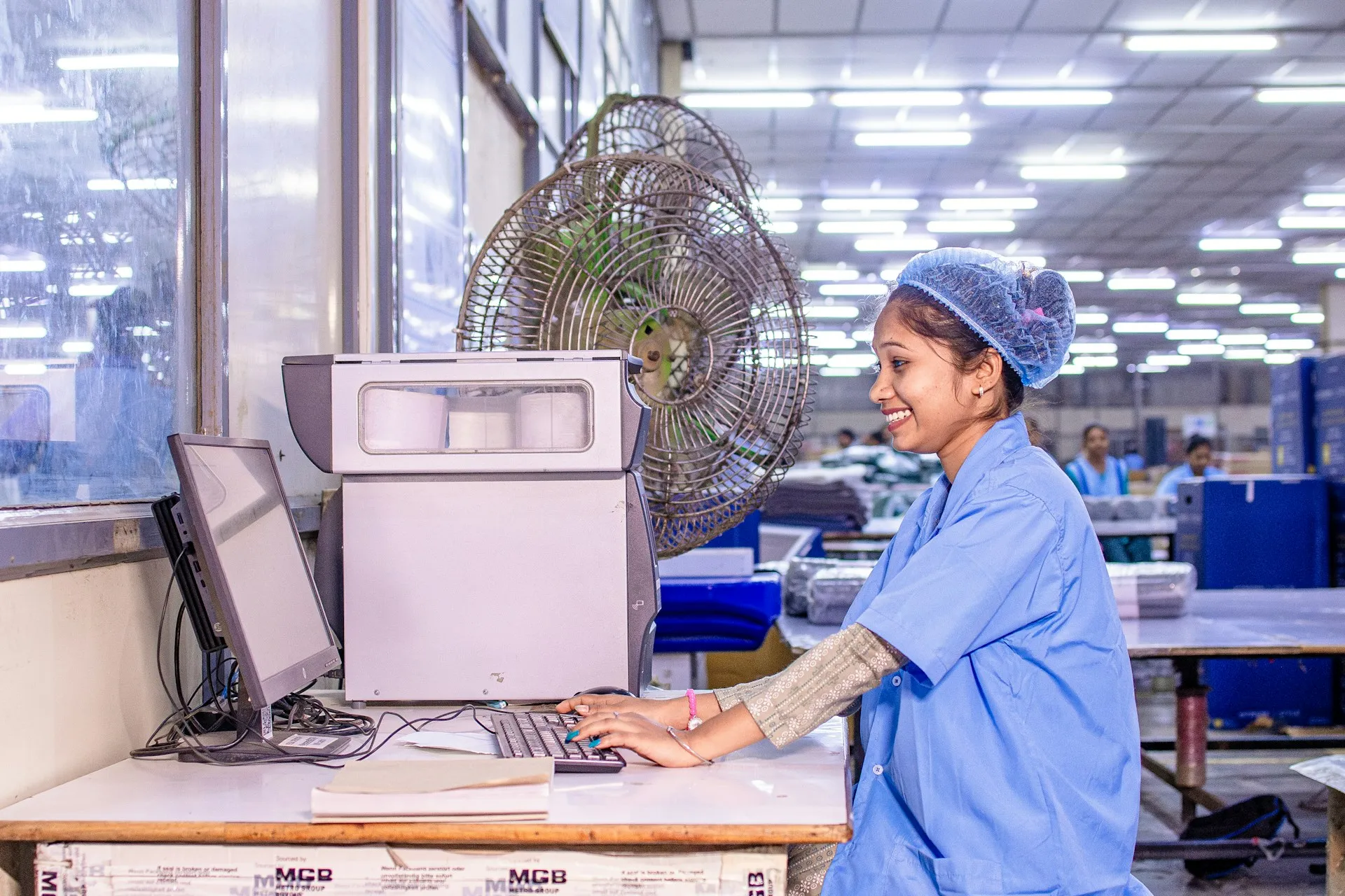Plant-floor records only help the service desk once they land in the CMDB it already works from; until then, an incident on this line starts with a phone call to controls. Smiling worker in a hairnet typing at a computer workstation on a large factory floor