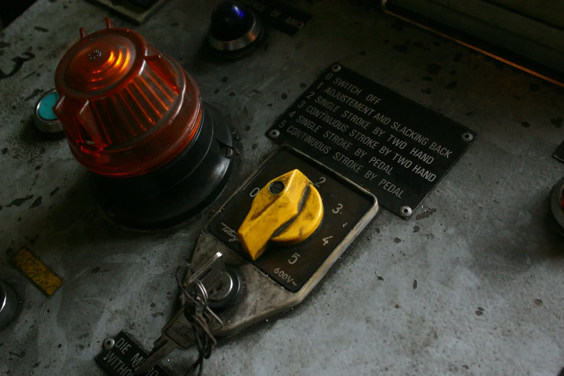 A running press cannot be rebooted on a patch schedule. That single fact is why OT vulnerability response has three options, not one. Worn machine control panel with an amber beacon, keyed yellow mode selector and engraved instruction plate