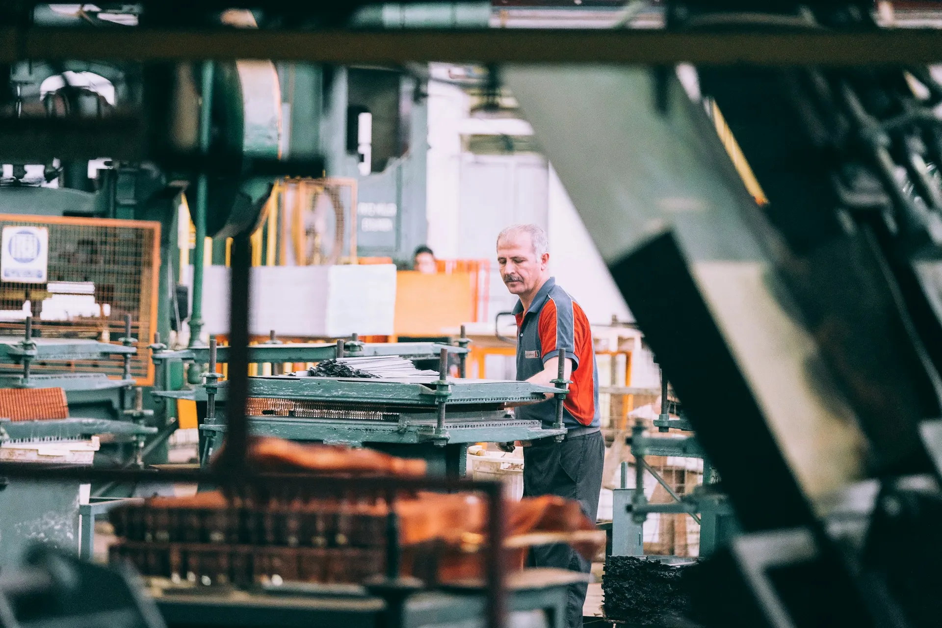 The approved-version model only works if the people who change machines on shift can follow it, so judge octoplant on the floor, not in the demo room. Worker in a red and grey shirt tending a press line in a busy metalworking shop