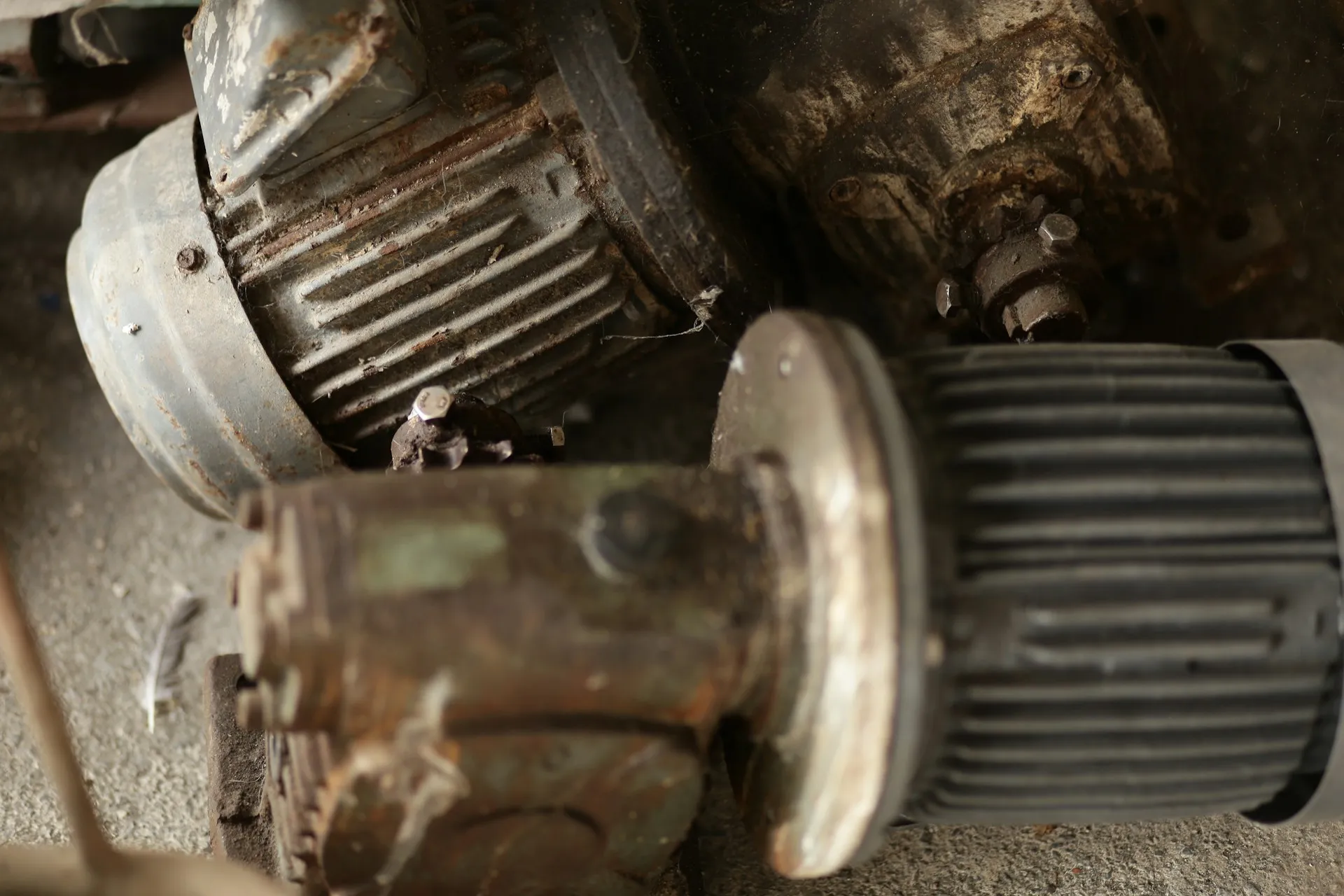 Every unit on this pile was once a supported part. A lifecycle signal is the cue to act while a spare and a backup still exist, not after the failure. Pile of rusted, worn electric motors and gearboxes lying on a concrete floor