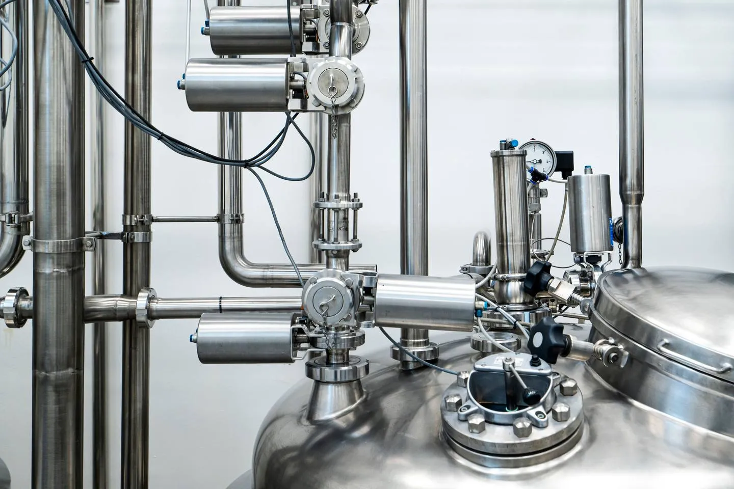 Sanitary valves, clamp fittings and instruments on a process vessel. In the product zone, every fitting and sensor has to be cleanable, not just waterproof. Stainless sanitary valves with pneumatic actuators, clamp fittings, a pressure gauge and a sight glass on top of a process vessel