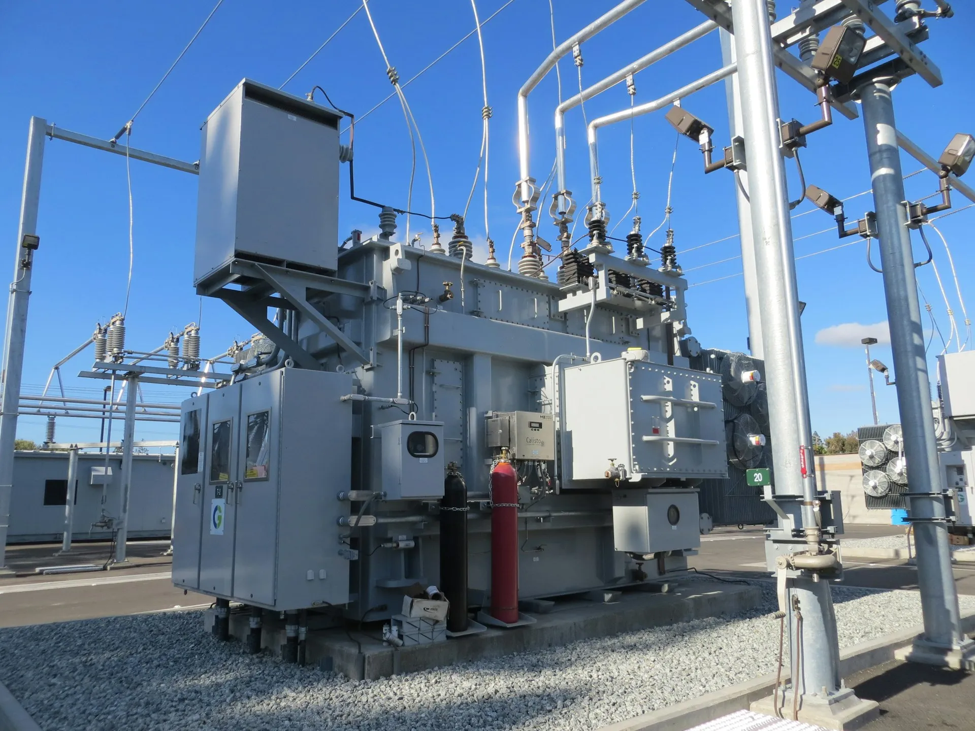 CIP scope follows the asset's impact rating: the same relay or controller can carry heavy CIP-010 duties at one substation and almost none at another. Substation power transformer with bushings, control cabinets and steel structures under a blue sky