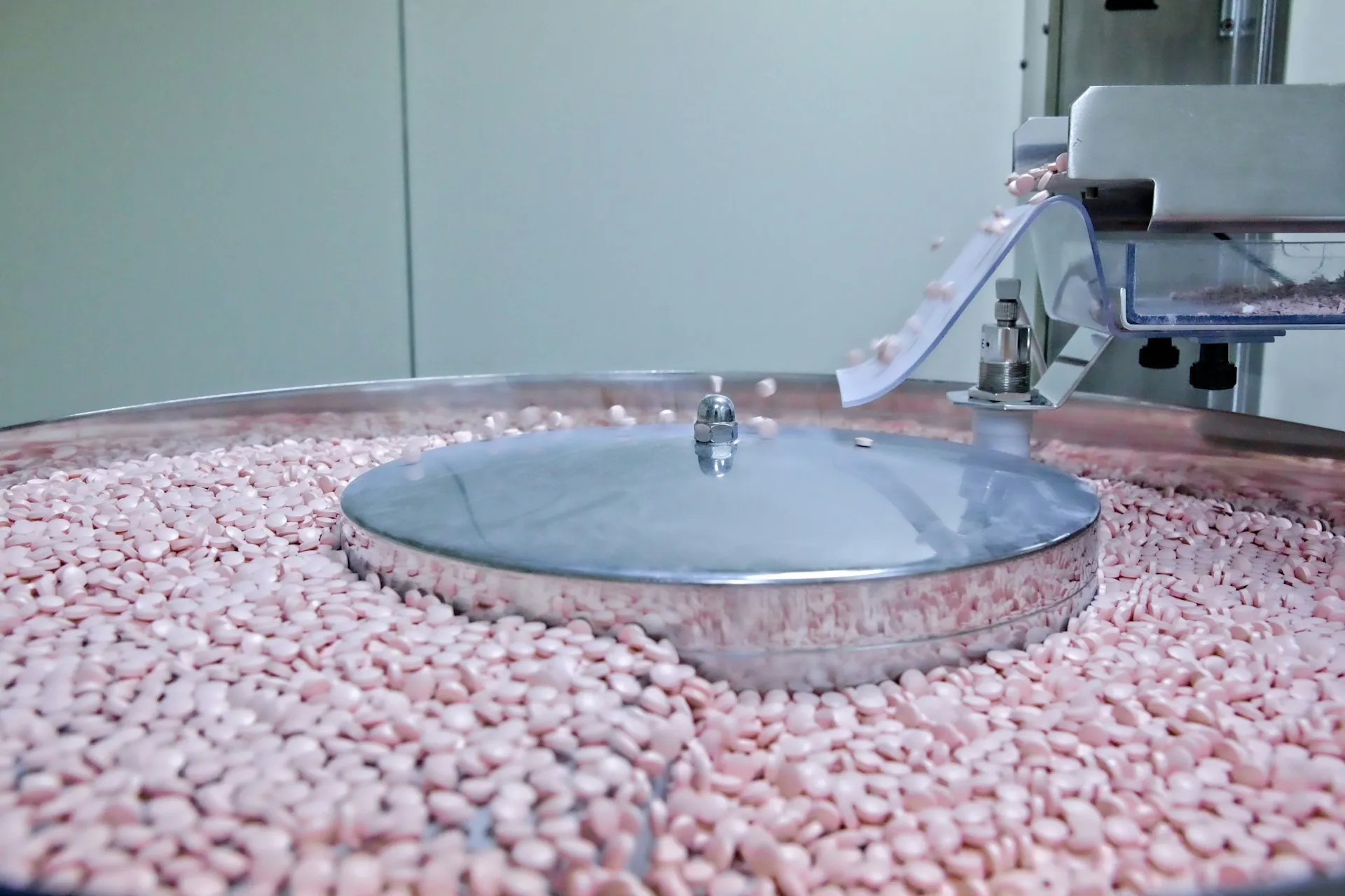 On GMP equipment like this tablet press, a changed reject timer is a change to the validated process, so the code change needs the same approved record as any other change. Pink tablets tumbling from a chute into the feeder bowl of a stainless tablet machine