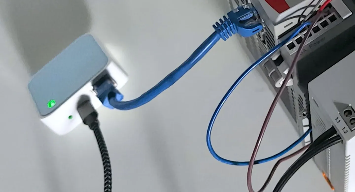 A travel router patched into a controller: a fair fix for a commissioning week, and an open door if it is still there a year later. A small travel router patched by Ethernet cable into a controller on a test bench