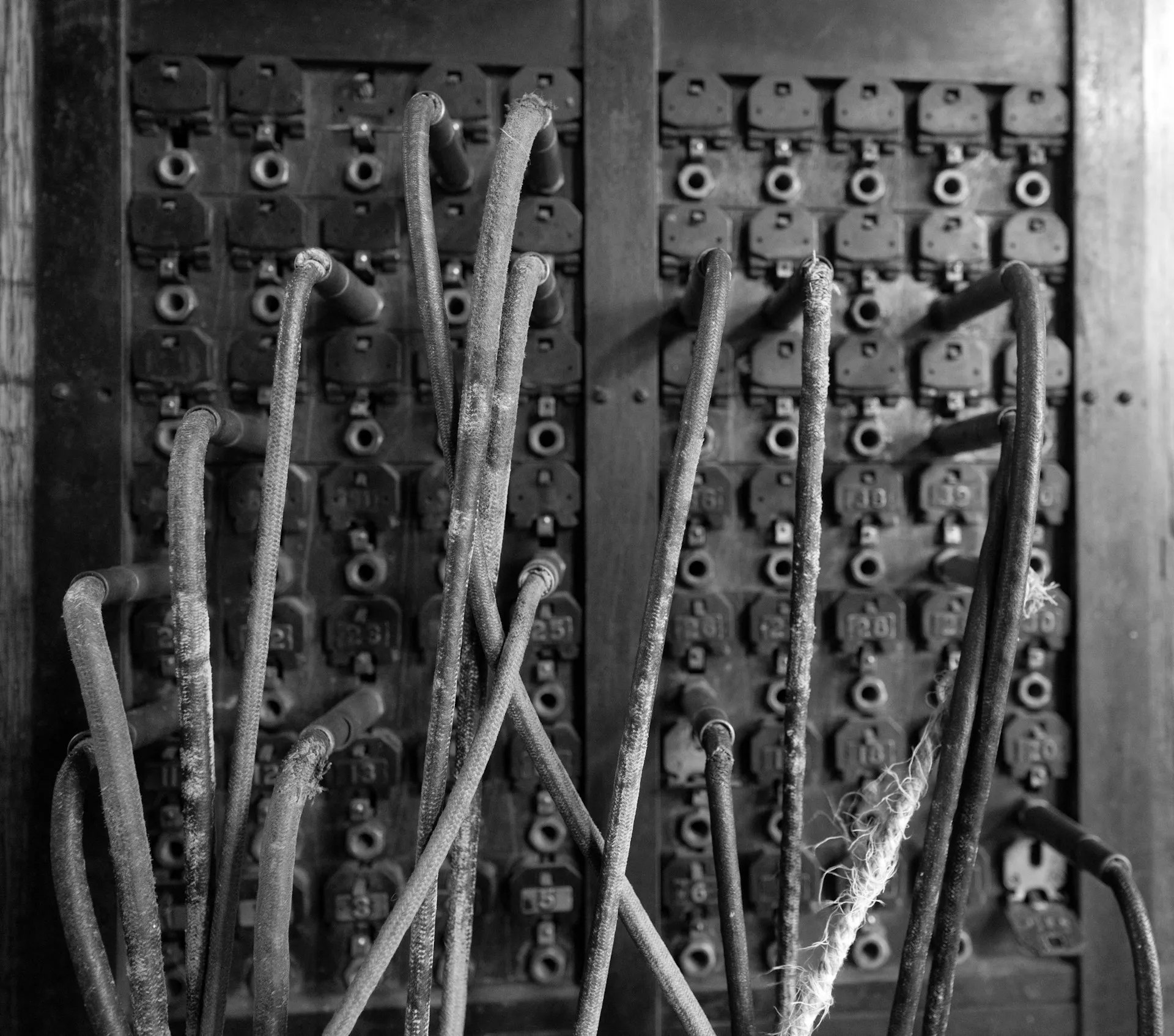A broker is a switchboard: senders and receivers each connect once to the middle, and nobody wires to anybody else directly. Black and white close-up of an old telephone switchboard with worn patch cords plugged into sockets