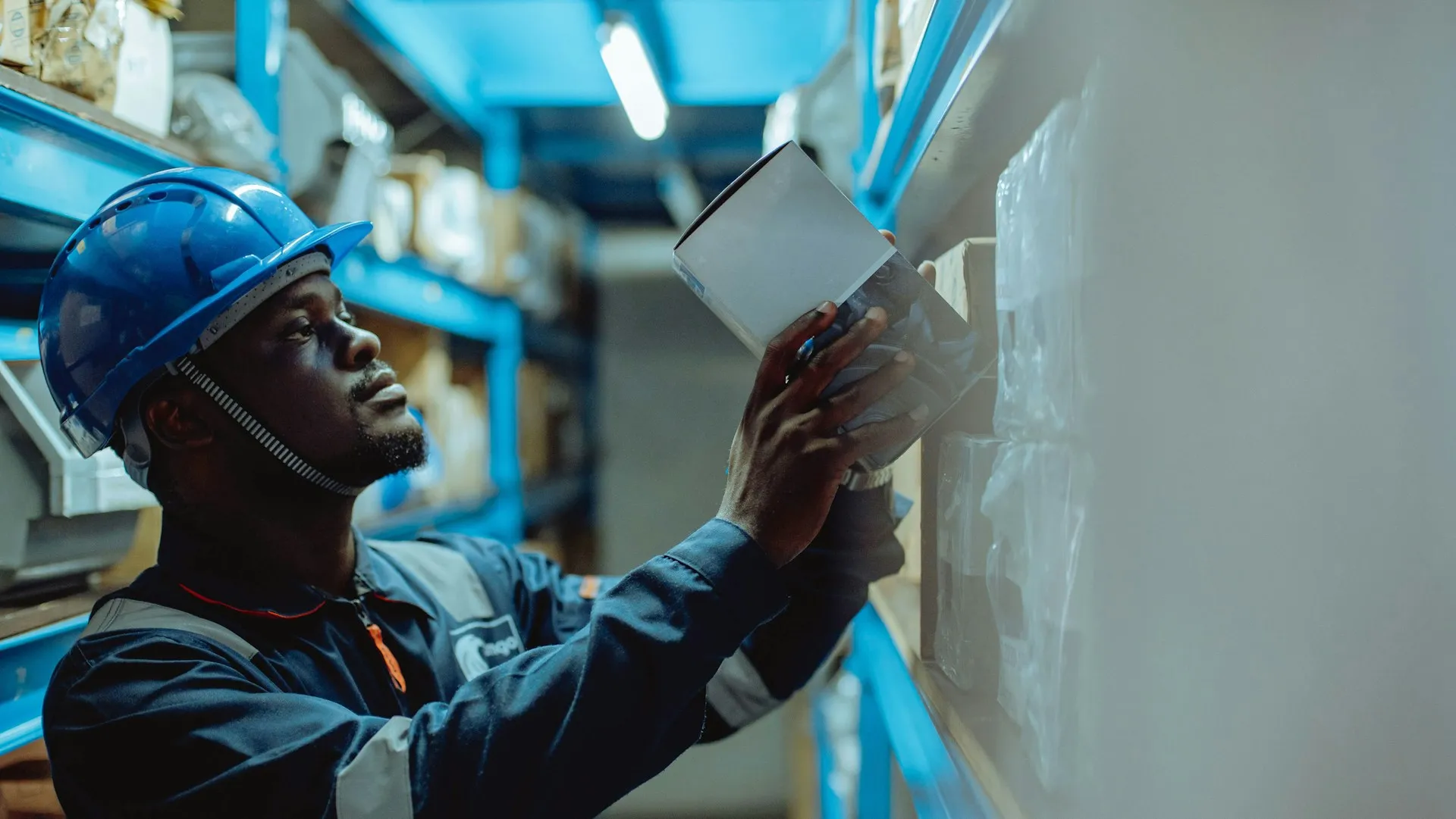 A goods movement scanned in the warehouse is an event that SAP and every downstream system needs to hear about immediately, rather than discover on the next polling cycle. Worker in a blue hard hat checking boxed stock on warehouse shelving with a handheld device
