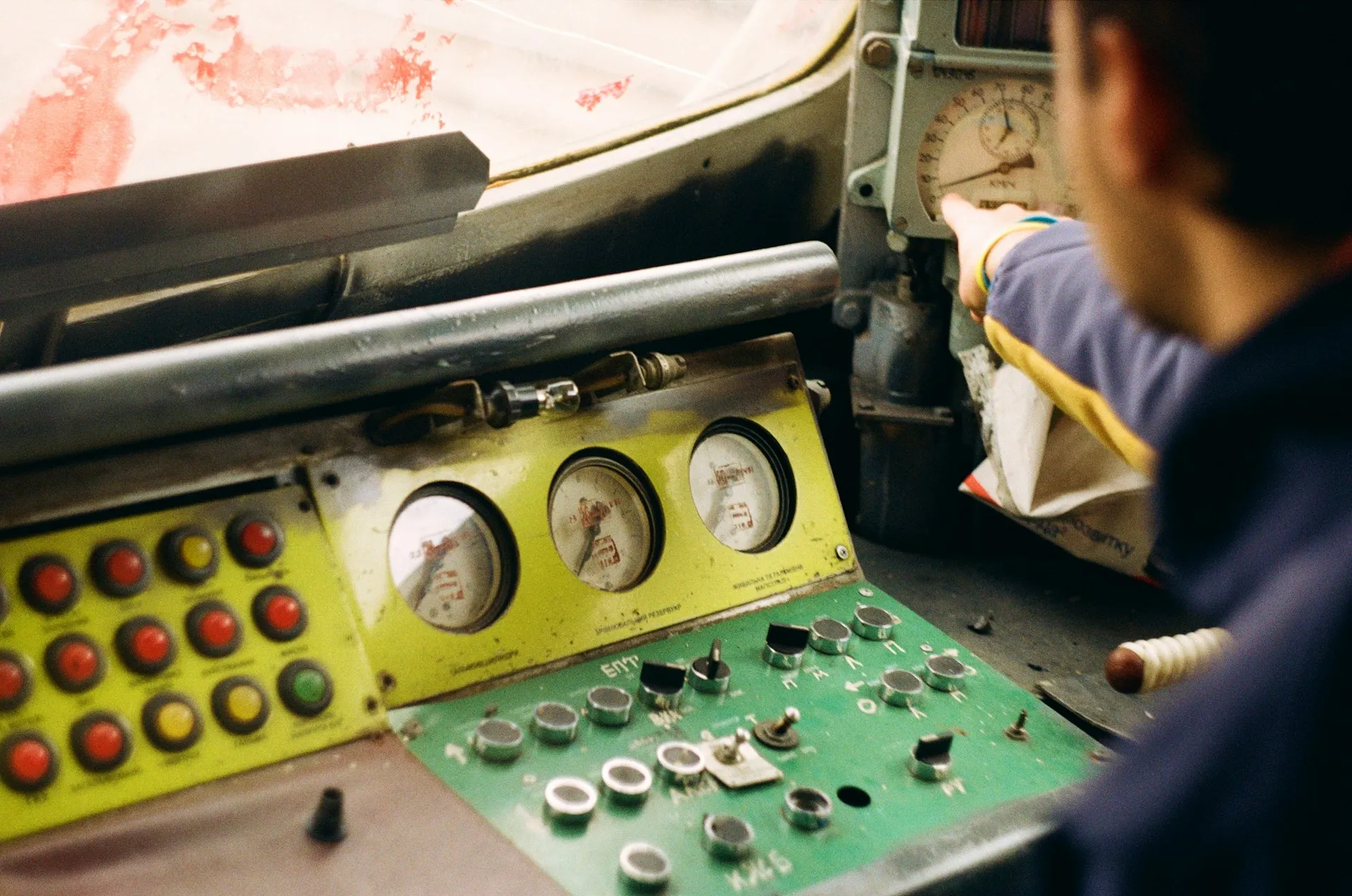 Worker reaching over an old machine console with gauges, coloured lamps and toggle switches