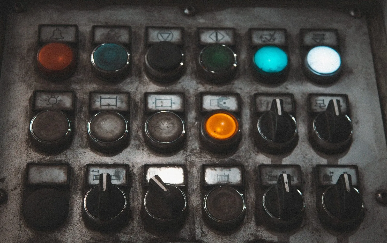 A worn machine control panel with rows of pushbuttons, pilot lights and selector switches