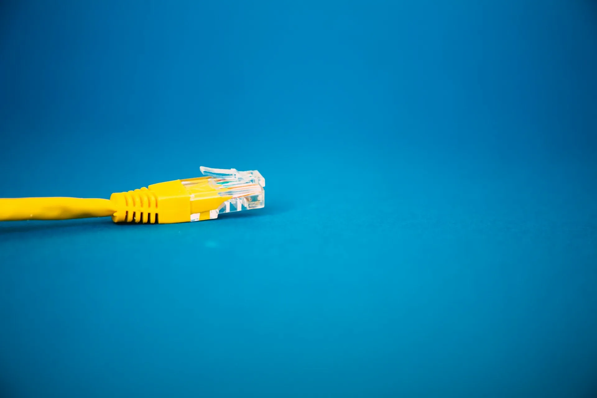 Open protocols work like a standard connector: any compliant client plugs in, and the broker can be changed later without rewriting the application. Single yellow network cable with its connector lying on a plain blue surface